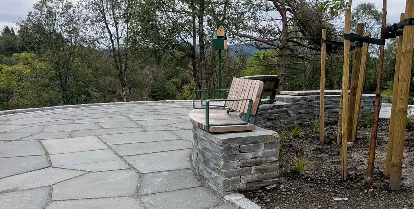Skiferlagt uteområde med natursteinsmur og integrerte sittebenker ved Skiftesvik gravplass.